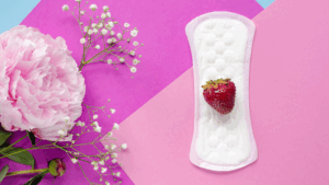 Imagem de uma flor e de um absorvente com um morango em cima, representado a microbiota vaginal.