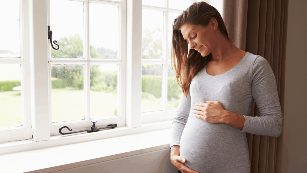 Mulher grávida sorrindo perto da janela, representando esperança e equilíbrio ao engravidar naturalmente após os 40.