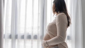 Mulher grávida olhando pela janela com expressão serena, refletindo sobre a fertilização in vitro e os possíveis riscos para o bebê.